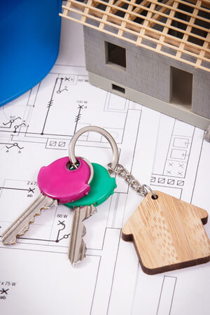 Keys With Home Shape And Small House Under Construction With Electrical Construction Drawings For Engineering Jobs. Building Home Cost